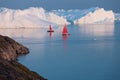 Little red sailboat cruising among floating icebergs in Disko Bay glacier during midnight sun season of polar summer. Greenland Royalty Free Stock Photo