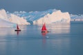 Little red sailboat cruising among floating icebergs in Disko Bay glacier during midnight sun season of polar summer. Greenland Royalty Free Stock Photo