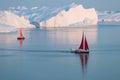 Little red sailboat cruising among floating icebergs in Disko Bay glacier during midnight sun season of polar summer. Greenland Royalty Free Stock Photo