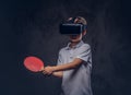 Little redhead boy dressed in a white t-shirt playing ping-pong with a virtual reality glasses. on dark Royalty Free Stock Photo