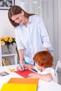 Little redhead boy with a nanny or mother or teacher sit at the table and paint with colors