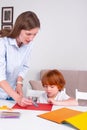 Little redhead boy with a nanny or mother or teacher sit at the table and paint with colors