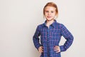 Little redhead girl in blue plaid shirt posing against wall. Royalty Free Stock Photo