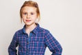 Little redhead girl in blue plaid shirt posing against wall. Royalty Free Stock Photo