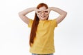 Little redhead girl playing superhero, making hand mask on eyes and smiling, having fun, standing over white background