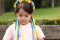 Little redhead preschooler girl with pigtails in national ukrainian folk decoration wreath outdoors