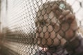 A little refugee girl with a sad look behind a metal fence. The social problem of refugees and internally displaced persons