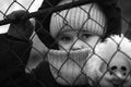 A little refugee girl with a sad look behind a metal fence. Social problem of refugees and internally displaced persons. Russia`s