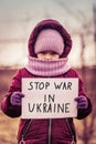 Little refugee girl with a sad look and a poster that says stop war in Ukraine. Social problem of refugees and internally
