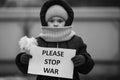 A little refugee girl with tears in her eyes and a placard that says please stop war. Social problem of refugees and internally