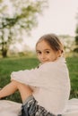 Little pretty tween girl in white clothes sitting on green grass outside in park on sunny summer day. Happy childhood and outdoor Royalty Free Stock Photo