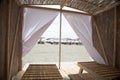 Little resting hut interior with white curtain and wooden benches at sandy beach.