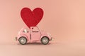 Little retro toy model car with red heart on pastel pink background. Love, friendship, valentines day, delivery