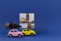 Little retro toy model cars with present gift box and small Christmas tree on navy blue background