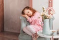 A little romantic girl with long hair sits on a chair in a children`s room and thinks about something