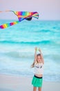 Little running girl with flying kite on tropical beach. Kid play on ocean shore. Child with beach toys. Royalty Free Stock Photo