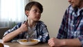 Little sad boy mixing cornflakes with spoon, looking at father, poor appetite Royalty Free Stock Photo