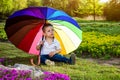 Little sad boy sitting under colorful umbrella in the garden Royalty Free Stock Photo
