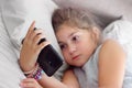 Little girl lying on the bed with her smartphone, being bored, watching alone