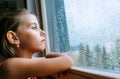 Little sad girl pensive looking through the window glass with a lot of raindrops. Sadness childhood concept image Royalty Free Stock Photo