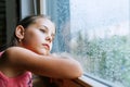 Little sad girl pensive looking through the window glass with a lot of raindrops. Sadness childhood concept image