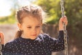 A little sad girl with pigtails rides on a swing in polka-dot clothes in a park against the background of foliage Royalty Free Stock Photo