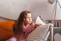 A little sad girl sits on a bed in the bedroom and looks out the window. children`s emotions. Melancholic mood