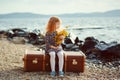 A little sad girl with a toy sitting on a big suitcase near the Royalty Free Stock Photo