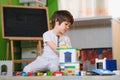 Little sad thoughtful bored toddler boy playing colorful building blocks alone at home during quarantine. development game.