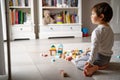 Little sad thoughtful bored toddler boy playing wooden colorful building blocks alone at home