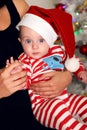 Little Santa baby posing beside Christmas tree at cozy home with New Year decoration,sitting at mom's hands Royalty Free Stock Photo