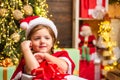 Little Santa Claus girl gifting gift. Funny kid holding Christmas gift. Cute little child near Christmas tree. Winter Royalty Free Stock Photo