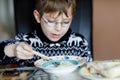 Little school boy with glasses eating vegetable soup indoor. Blond child in domestic kitchen or in school canteen. Cute Royalty Free Stock Photo