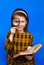 Little school girl in checkered dress holding magnifier and smiling Royalty Free Stock Photo
