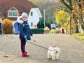 Little school girl playing with little maltese puppy outdoors after school. Happy child and family dog having fun