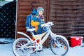 Little school kid boy of elementary class walking to school during snowfall. child removing snow from bicycle.