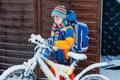 Little school kid boy of elementary class walking to school during snowfall. child removing snow from bicycle. Student