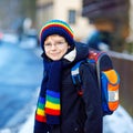 Little school kid boy of elementary class walking to school during snowfall. Happy healthy child with glasses having fun