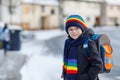 Little school kid boy of elementary class walking to school during snowfall. Happy healthy child with glasses having fun