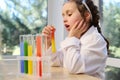 Little schoolgirl observing the chemical reaction standing at the table with test tubes on tripode on a chemistry lesson