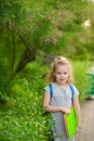 The little schoolgirl stand on background park vegetation.