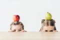 little schoolgirls with apple and pear on heads hiding behind table