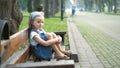 Little serious child girl sitting alone on a bench in summer park Royalty Free Stock Photo