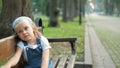 Little serious child girl sitting alone on a bench in summer park Royalty Free Stock Photo