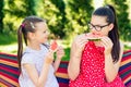 Little sisters eating watermelon slices in the garden sitting on a hammock