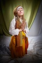 Little skinny praying girl in long white and yellow dress with scarf on head. Young model posing for photo shoot in dark