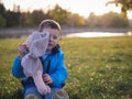 Little Slavic joyful boy on the lawn portrait in the spring in a city park with a soft toy