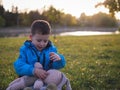 Little Slavic joyful boy on the lawn portrait in the spring in a city park with a soft toy