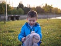 Little Slavic joyful boy on the lawn portrait in the spring in a city park with a soft toy