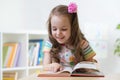 Little smart girl looking at book while sitting on chair in nursery Royalty Free Stock Photo